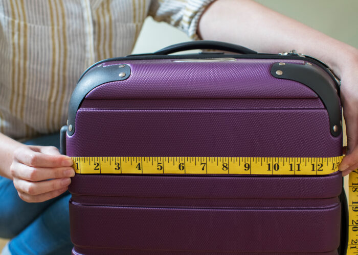 Close up of woman measuring a purple carry on suitcase with a yellow measuring tape