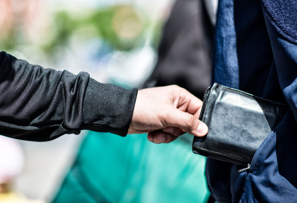 Close up of person stealing wallet from another person's shoulder bag