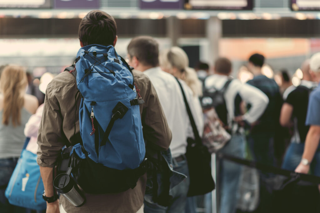 Young person with backpack waiting to check in for flight at busy airport