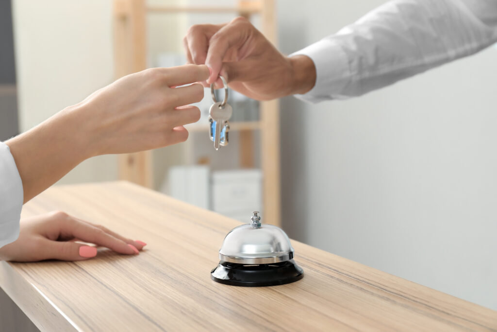 Close up of person handing over a set of keys over a hotel front desk with a bell on it