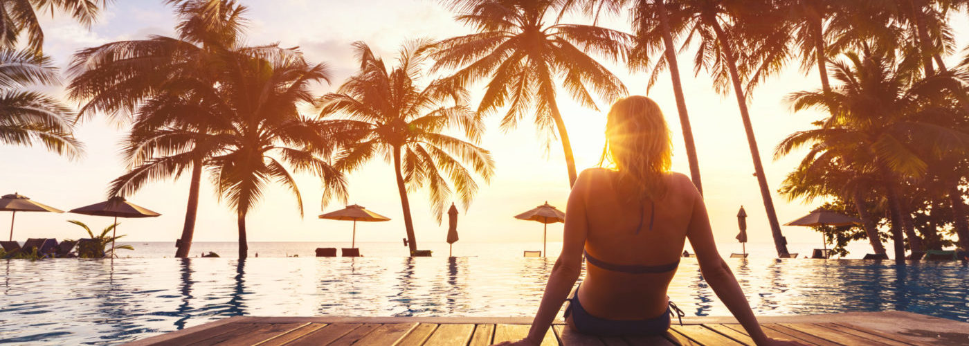 Woman relaxing on a pier in front of a pool and palm trees