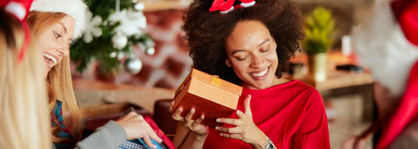 Friends giving and opening Christmas presents next to Christmas tree