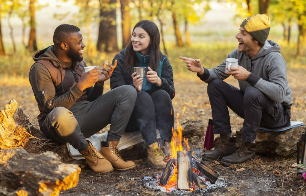 Three friends laughing around a campfire