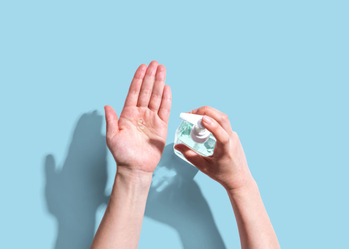 Bird's eye view of person sanitizing their hands on a light blue backdrop