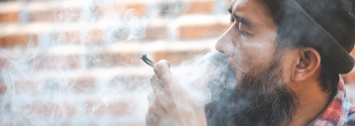 Man smoking a marijuana joint in front of a brick wall