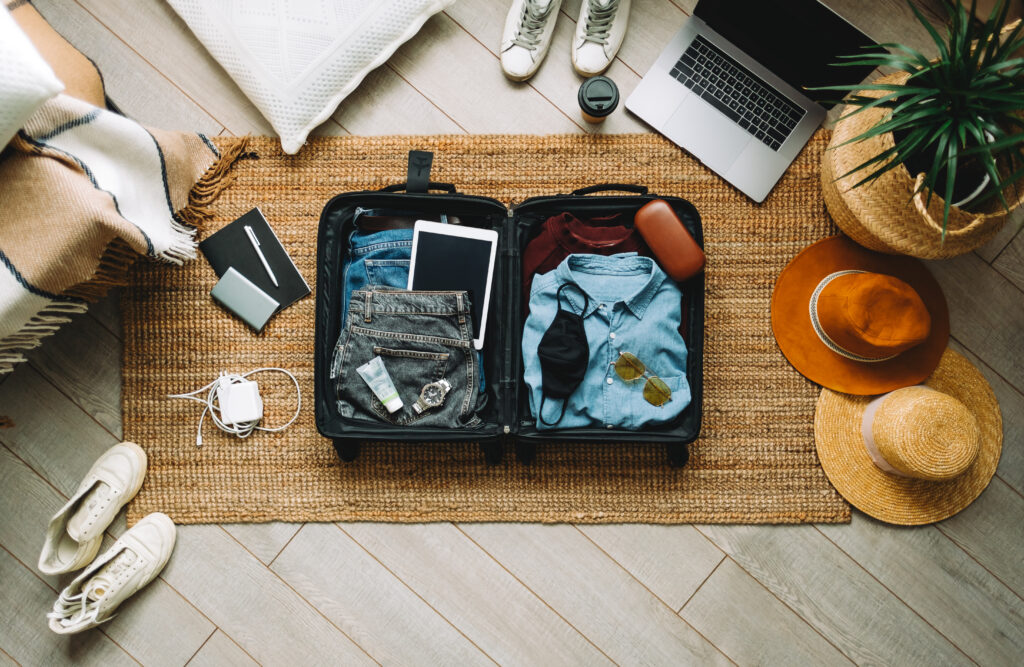 Overhead view of open suitcase filled with clothes, travel gear, and technology