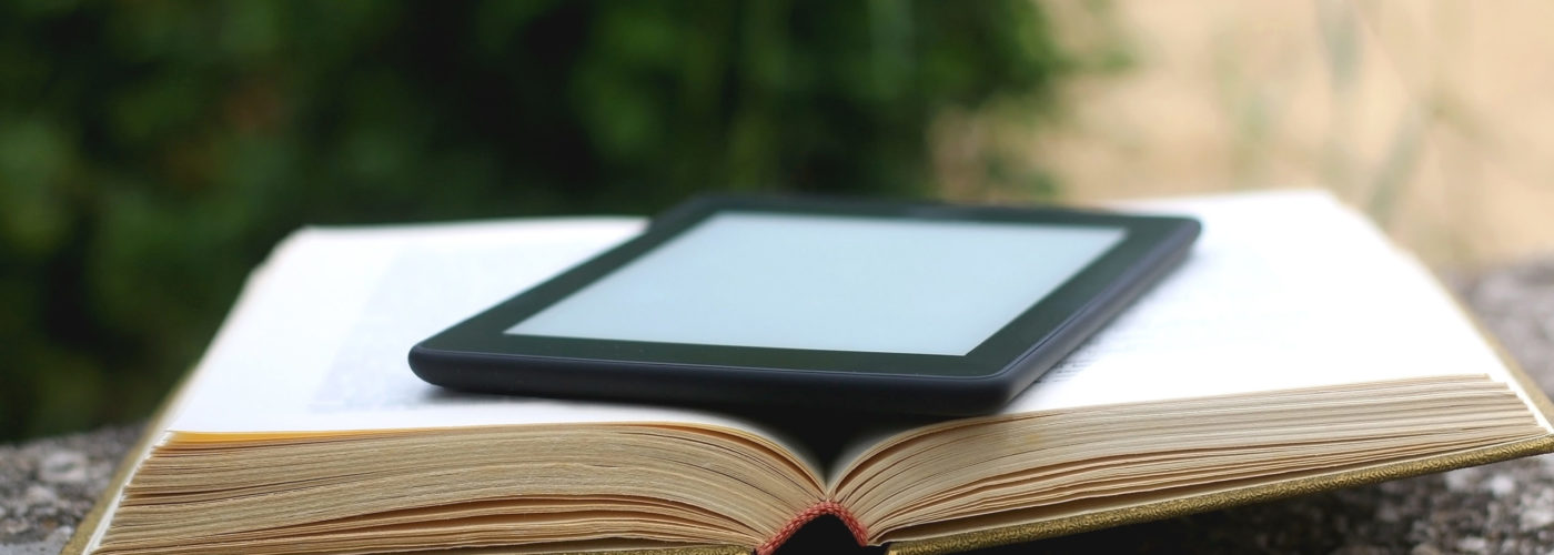 eReader laying on top of an open paper book outside on a cement ledge