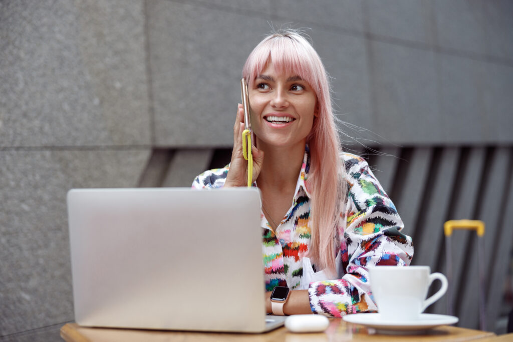 Woman talking on phone at cafe with laptop and cup of coffee