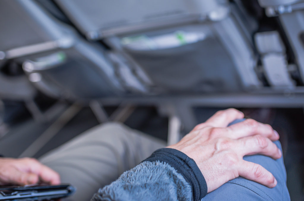 Close up of hand gripping knee on airplane, showing flight anxiety