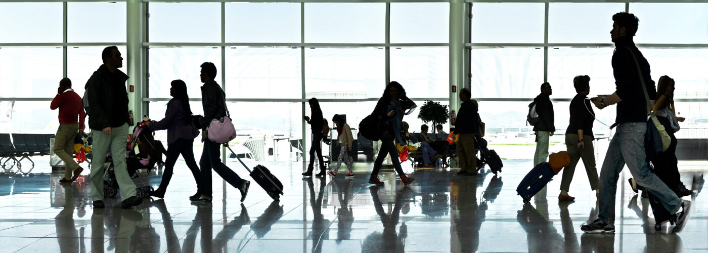 Silhouettes of people walking past a large window in an airport terminal